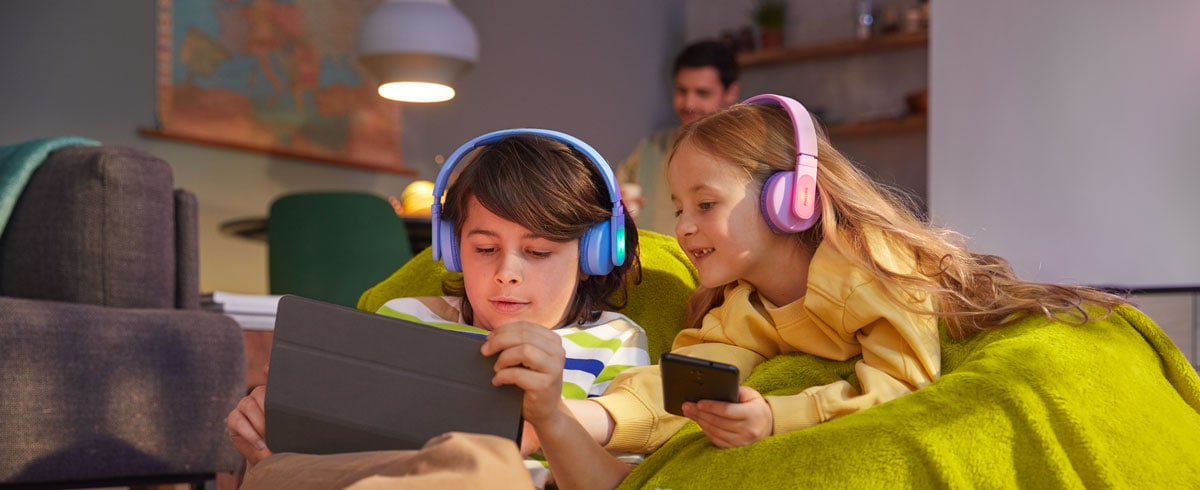 Egy fiú és egy lány használja készülékét, miközben tartós gyerekfejhallgatót használ