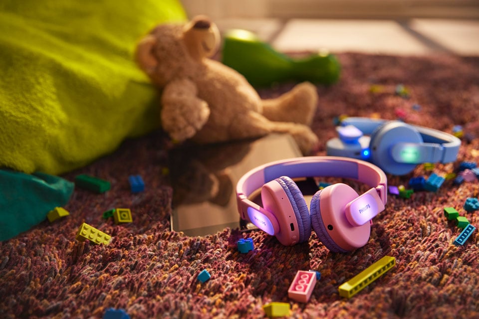 Egy kék és egy rózsaszín gyerekfejhallgató a földön játékokkal