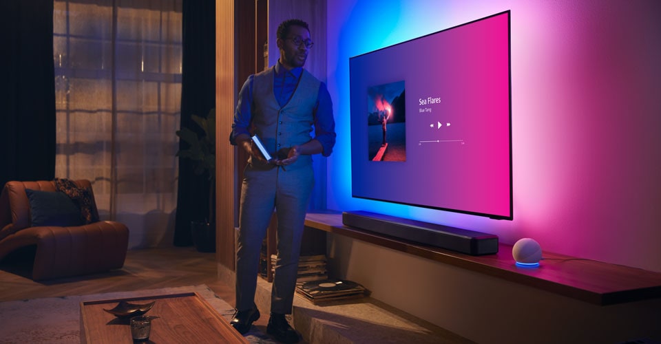 Egy személy egy modern nappaliban egy Philips Ambilight TV közelében, zenei interfészével és Fidelio soundbarral