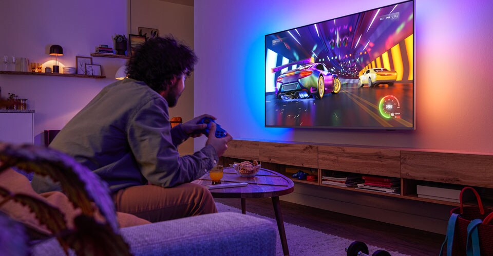 Egy személy a kanapén ül, és egy autóversenyzős videojátékot játszik egy Philips Ambilight tévén