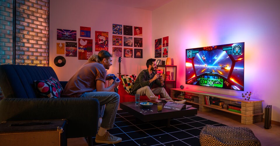 Két ember lelkesen játszik egy űr témájú videojátékkal egy hangulatos, színes nappaliban