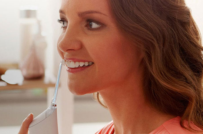Egy nő hófehér fogait mossa egy Philips Sonicare Airfloss elektromos fogkefével. 